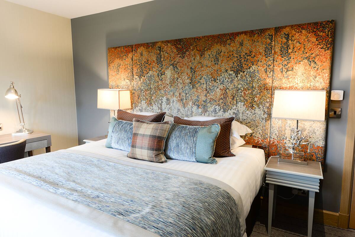 A hotel room with a large bed, two bedside tables with lamps, a decorative tapestry on the wall, and a patterned bedspread.