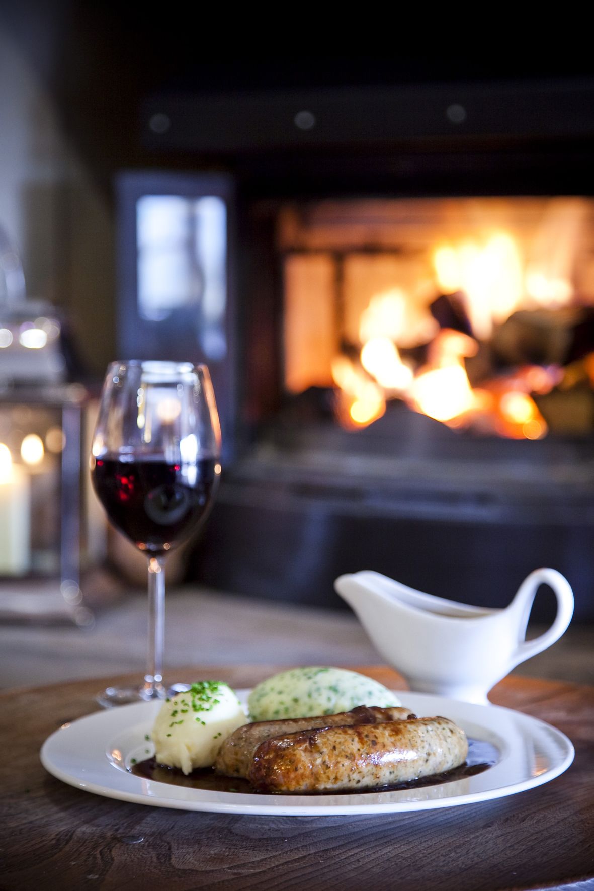 Une assiette remplie de nourriture et un verre de vin rouge sont posés sur une table en bois, avec une cheminée en arrière-plan.