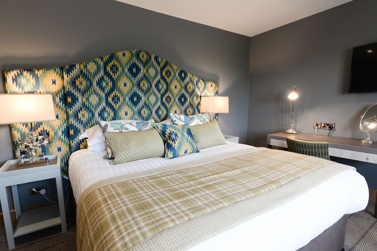 A hotel room with a large bed, two bedside tables with lamps, a desk with a chair, and a mounted TV.