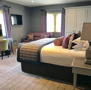 Une chambre d’hôtel avec un grand lit, un canapé, un téléviseur fixé au mur et un bureau avec une lampe.