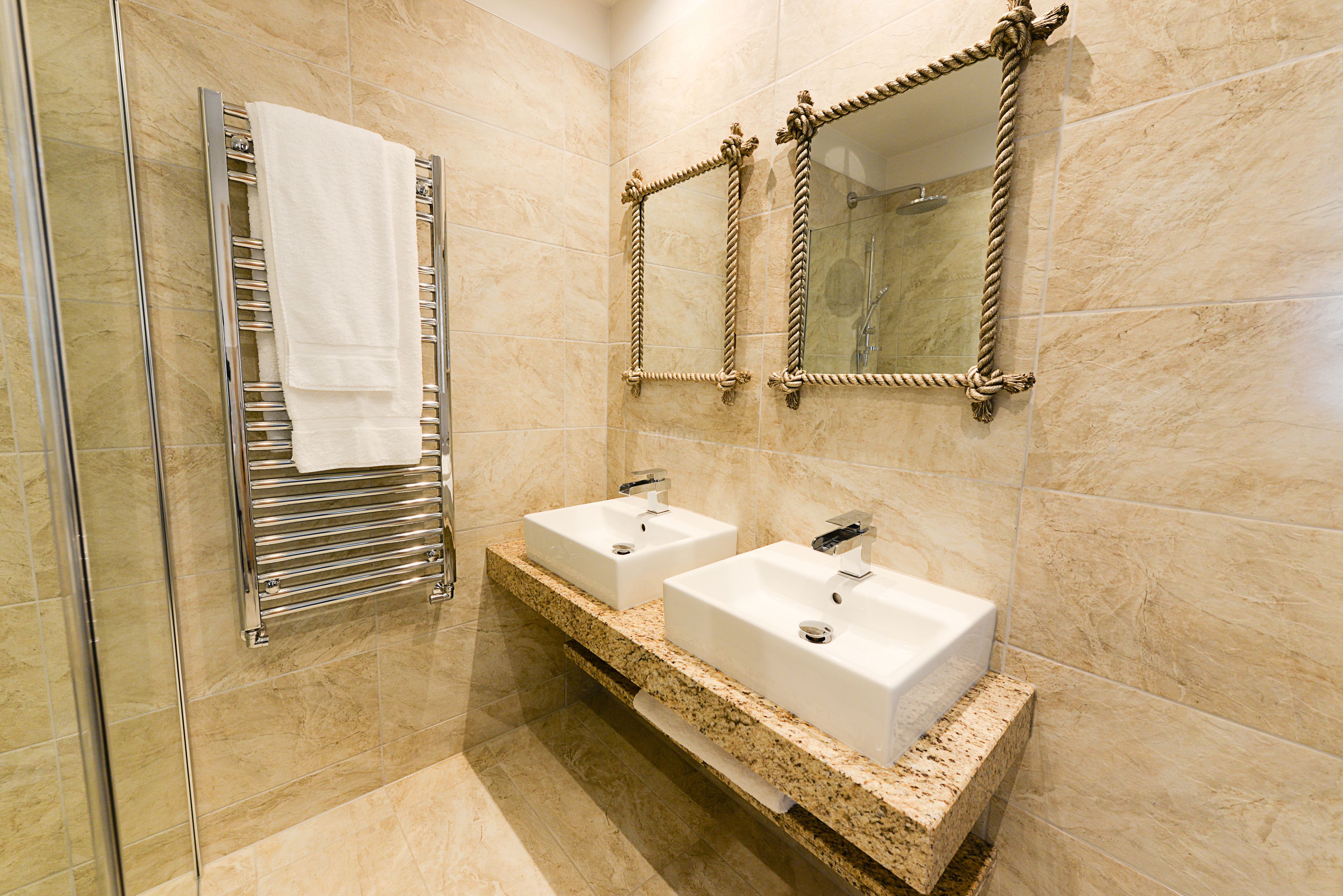 A modern bathroom with two sinks, a towel rack, and a mirror with rope decoration.