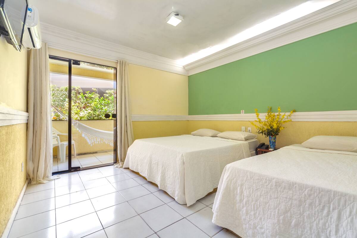 A hotel room with two beds, a green wall, and a view of greenery outside.