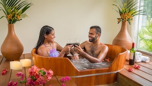A wooden bathtub with two people toasting with wine glasses, surrounded by flowers and candles. - Floral Inn Family Hotel (Porto Seguro)