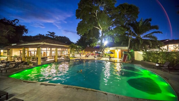 A swimming pool with green lighting, surrounded by lounge chairs and a covered area with tables and umbrellas. - Floral Inn Family Hotel (Porto Seguro)