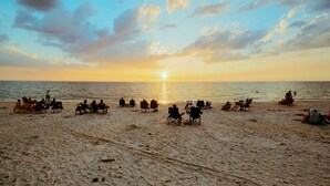 A beach with people sitting on chairs facing the ocean during sunset. - Floral Inn Family Hotel (Porto Seguro)