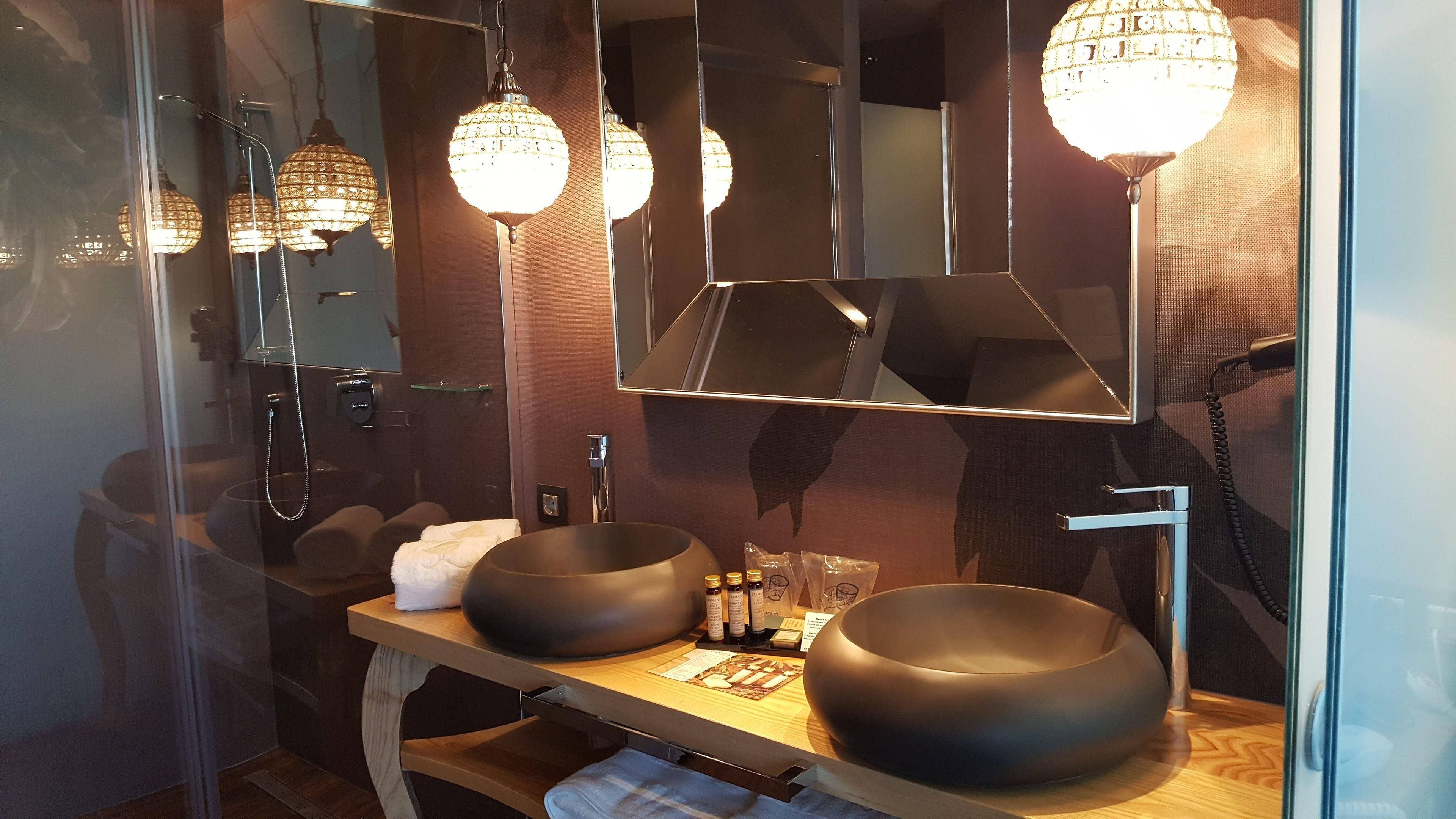 A modern bathroom with two large black sinks, a mirror, and decorative crystal lights.
