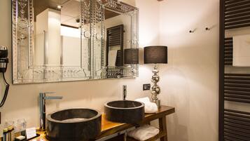A bathroom with two large, round sinks, a mirror with ornate framing, a towel rack, and a lamp.