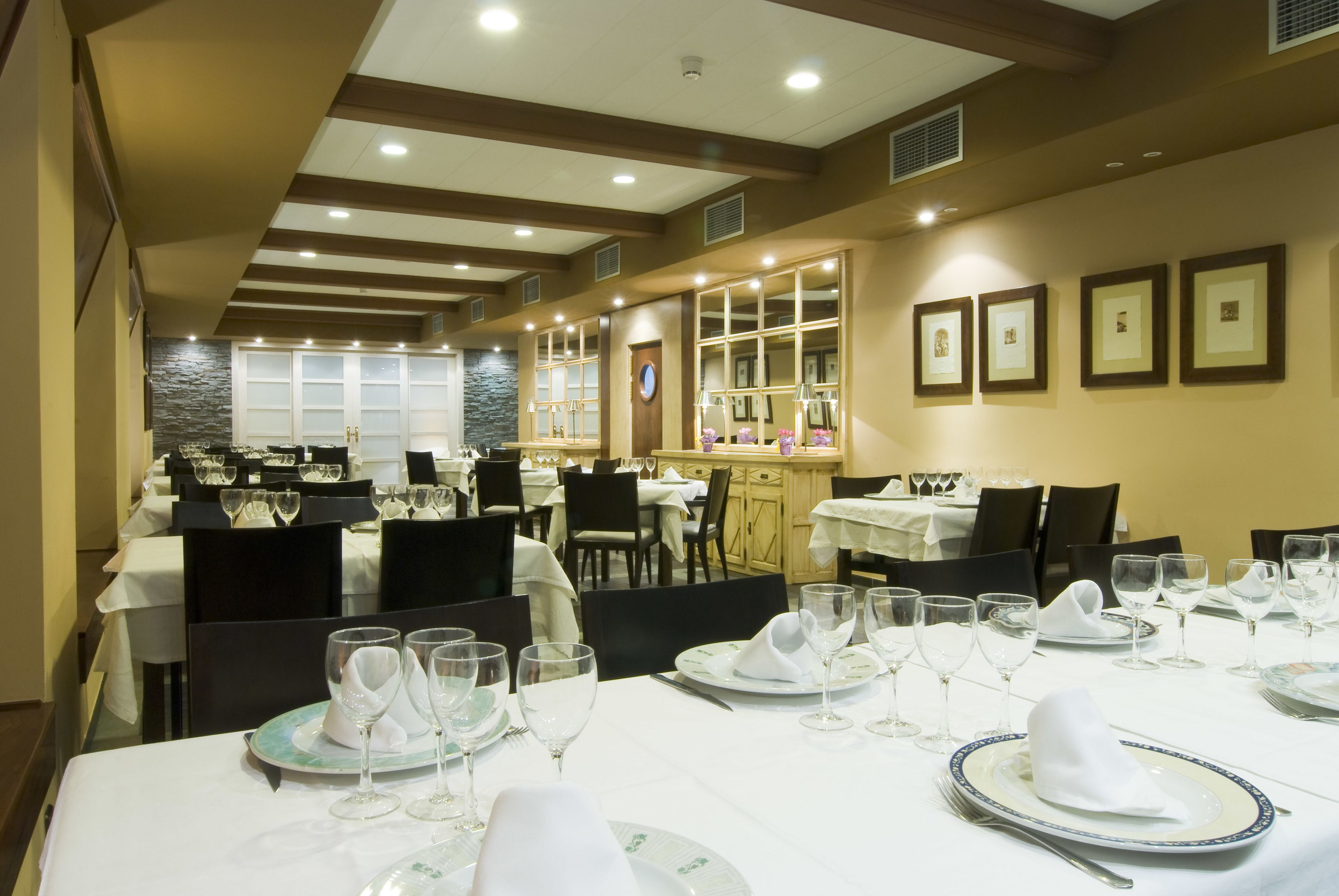 Un restaurante con varias mesas dispuestas para comer, con manteles blancos y cubertería ordenada.