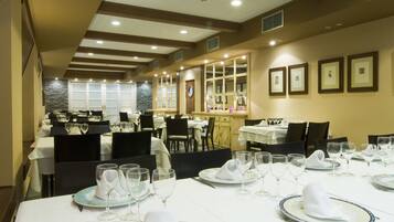Un restaurante con varias mesas dispuestas para comer, con manteles blancos y cubertería ordenada.