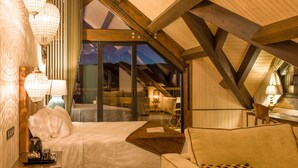 A cozy room with a bed, a sofa, and a large window offering a view of the mountains. - Alojamientos Ainsa Sanchez (Ainsa)