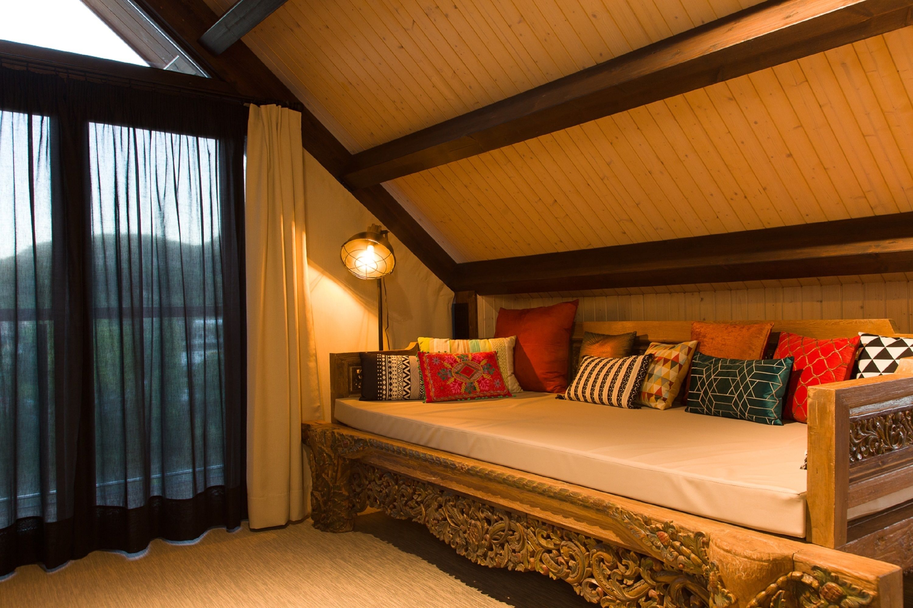 A cozy bedroom with a sloped ceiling, a bed with multiple pillows, and a window with curtains.