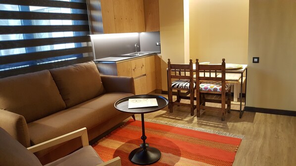 A compact living space with a sofa, a dining table with chairs, a small kitchen area, and a patterned rug. - Alojamientos Ainsa Sanchez (Ainsa)