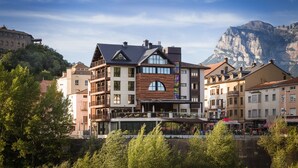 A multi-story hotel with balconies, a central courtyard, and a mountain backdrop. - Alojamientos Ainsa Sanchez (Ainsa)