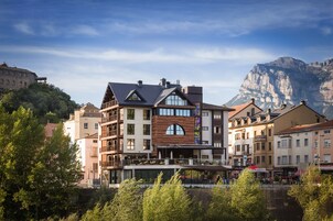 Un hotel de varios pisos con balcones, un patio central y montañas al fondo.