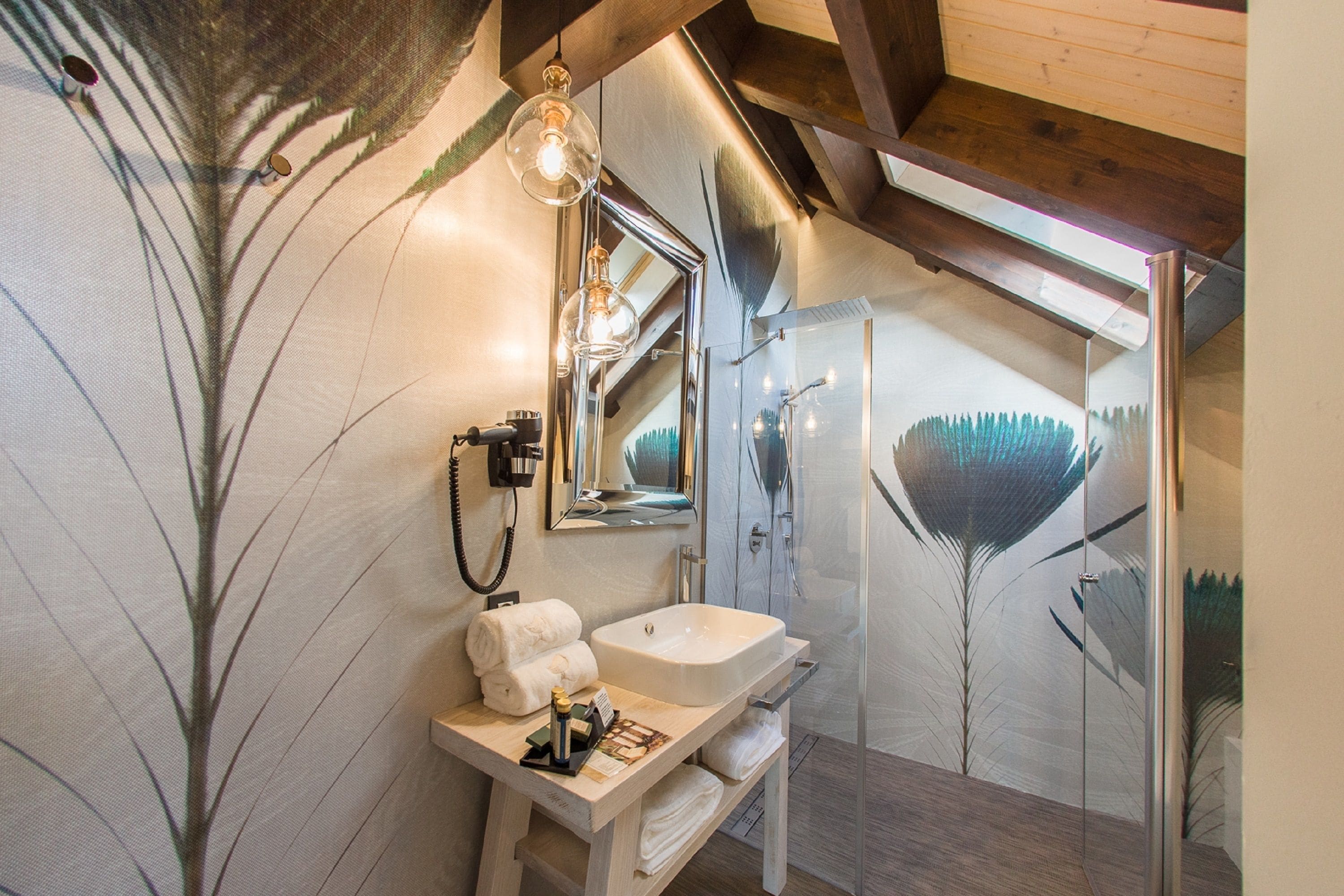 A modern bathroom with a white sink, a mirror, and a shower. There are towels and toiletries on the sink counter.