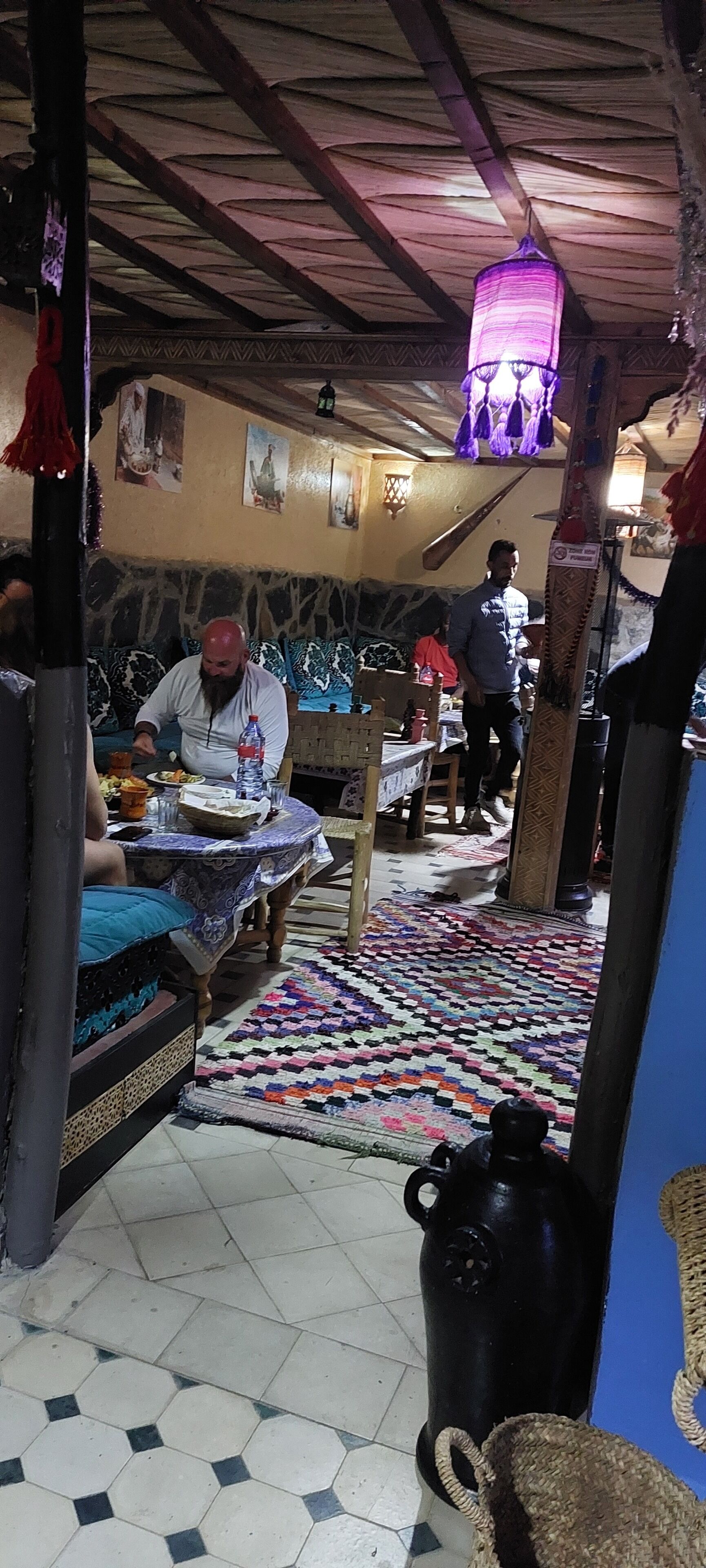 Un coin repas agrémenté d’un tapis à motifs, d’une table recouverte d’une nappe bleue et d’une lanterne violette suspendue.