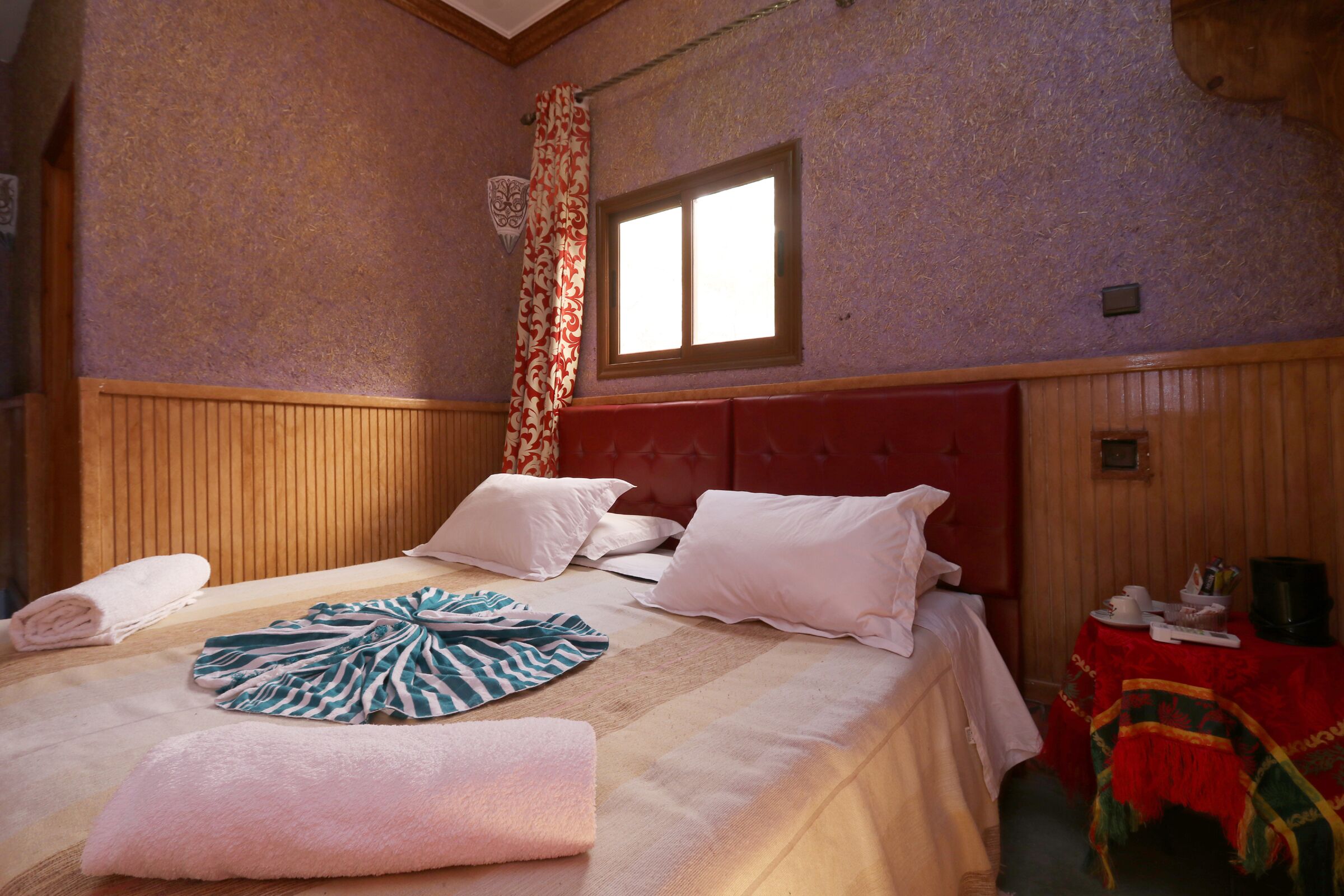 Habitación de hotel con una cama grande, cabecero de madera y una ventana con cortinas.