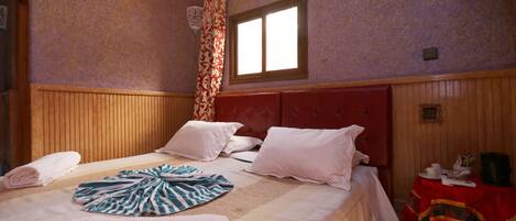 Habitación de hotel con una cama grande, cabecero de madera y una ventana con cortinas.