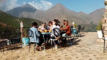 Un grupo de personas cenando en una mesa al aire libre con vistas a la montaña.
