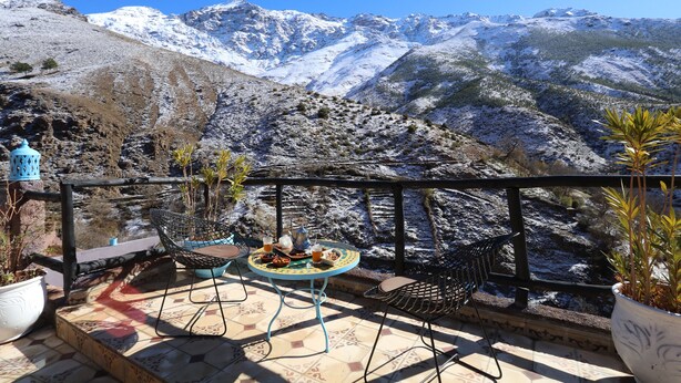 A terrace with a table and chairs, overlooking a snow-covered mountain range. - Toubkal Garden Hotel (Asni)