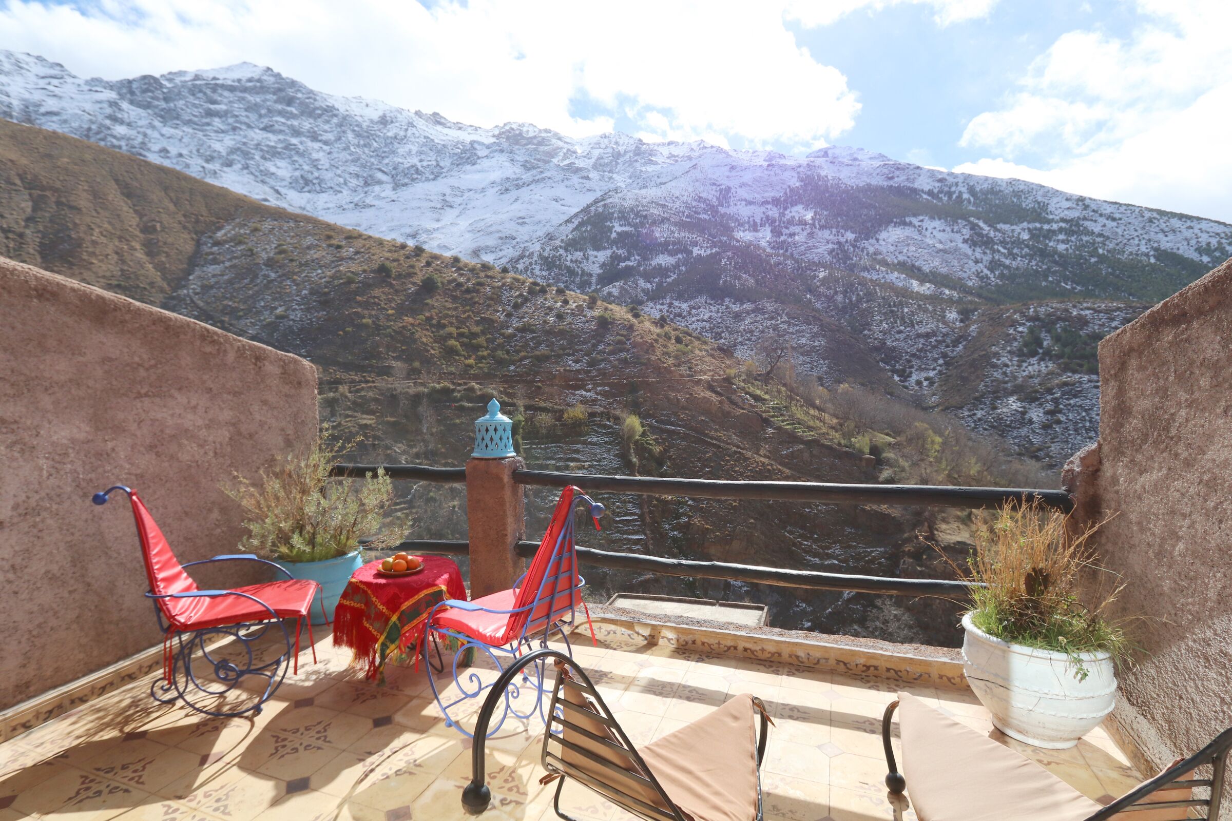 Una terraza con dos sillas rojas, una mesa con naranjas y una planta en maceta.