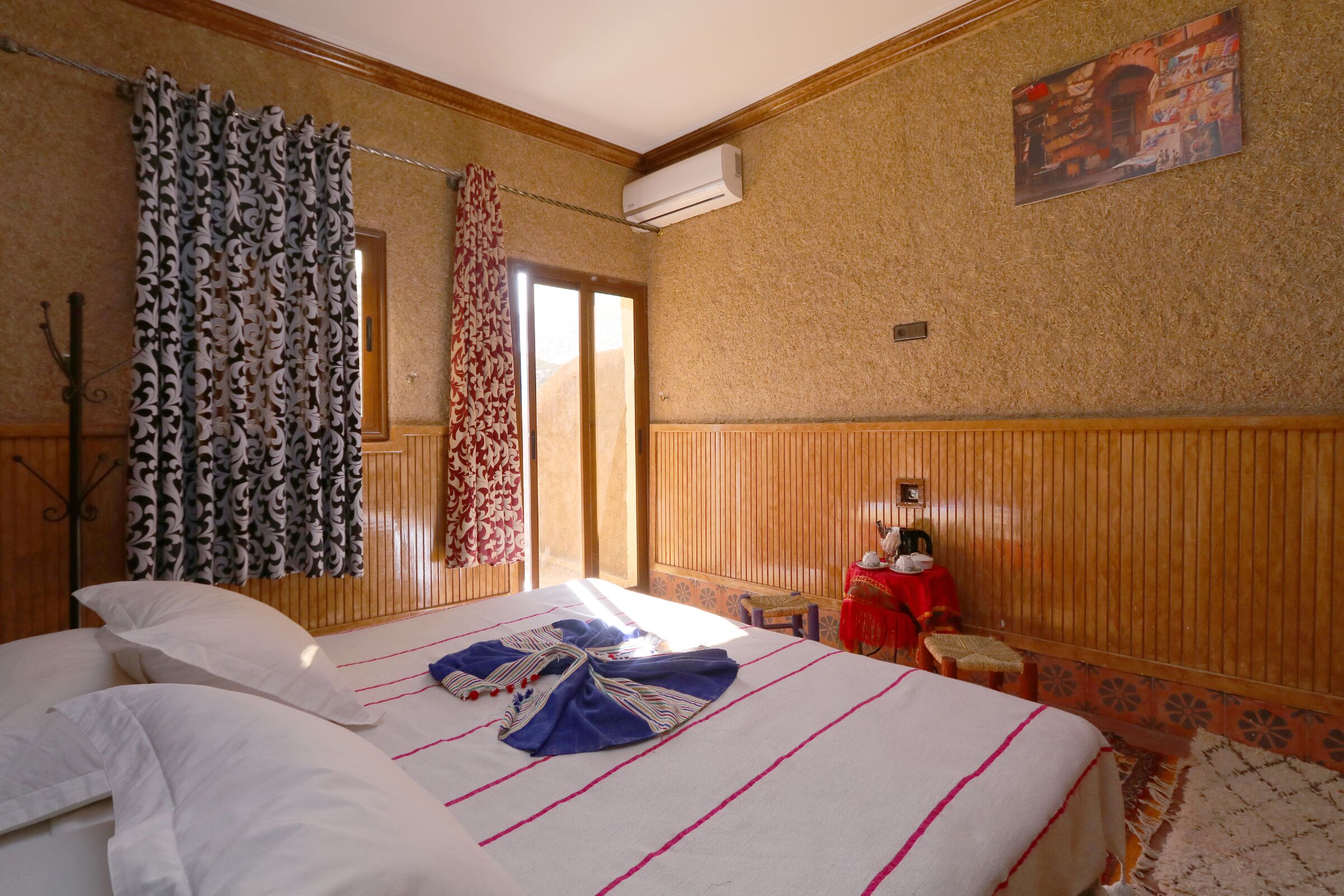 Habitación de hotel con cama, una mesita, una silla, ventana con cortinas y aire acondicionado de pared.