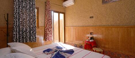 Habitación de hotel con cama, una mesita, una silla, ventana con cortinas y aire acondicionado de pared.