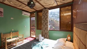 A room with a bed, a bench, a window with a view of mountains, and an air conditioning unit. - Toubkal Garden Hotel (Asni)