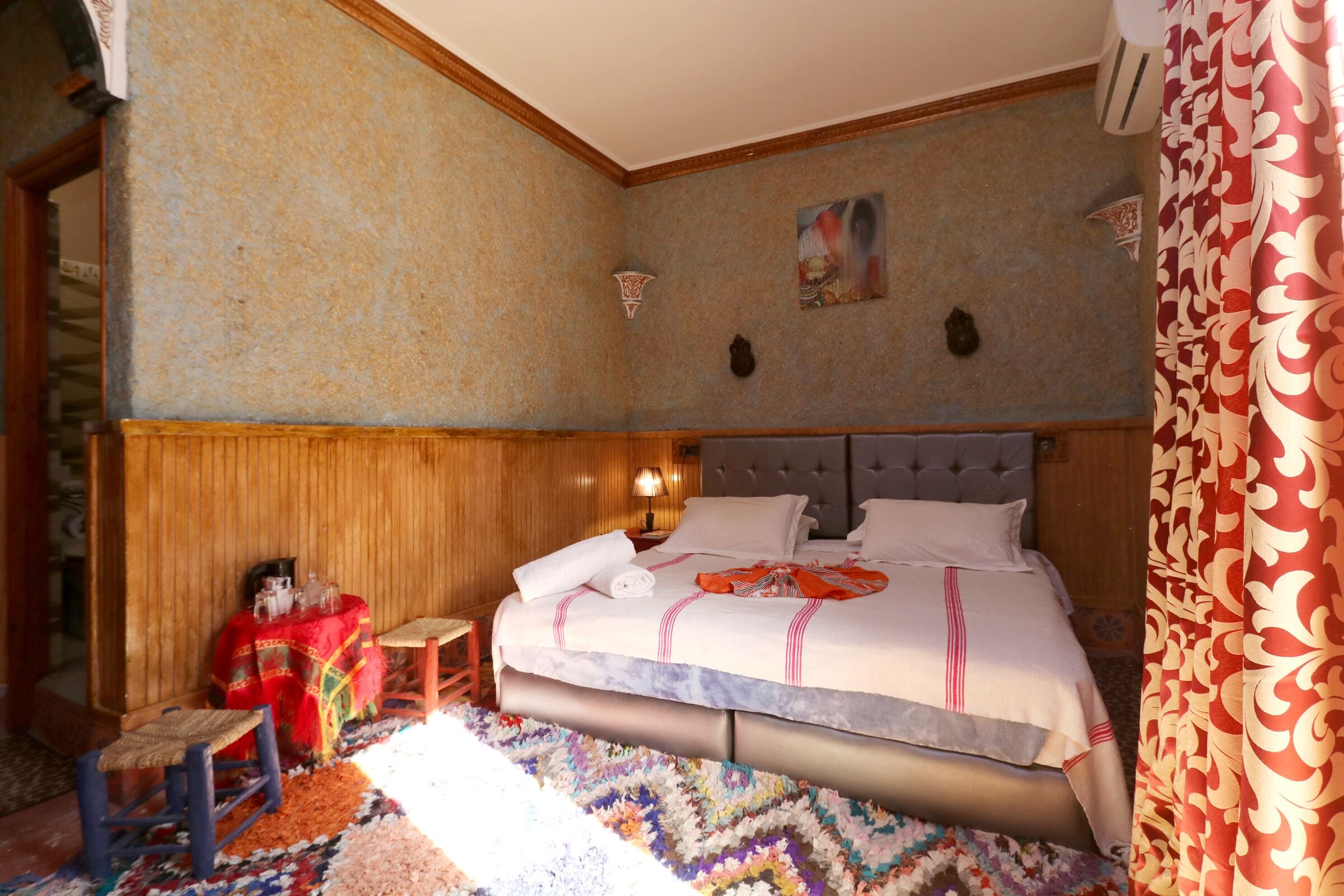 A bedroom with a large bed, a small table, a chair, and a patterned rug.
