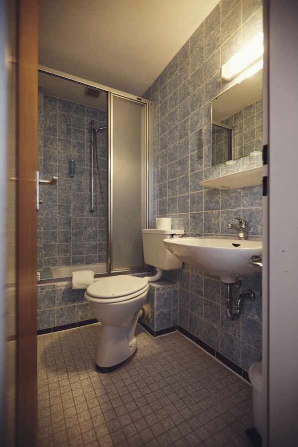 Baño con ducha, inodoro, lavamanos y paredes de azulejos.