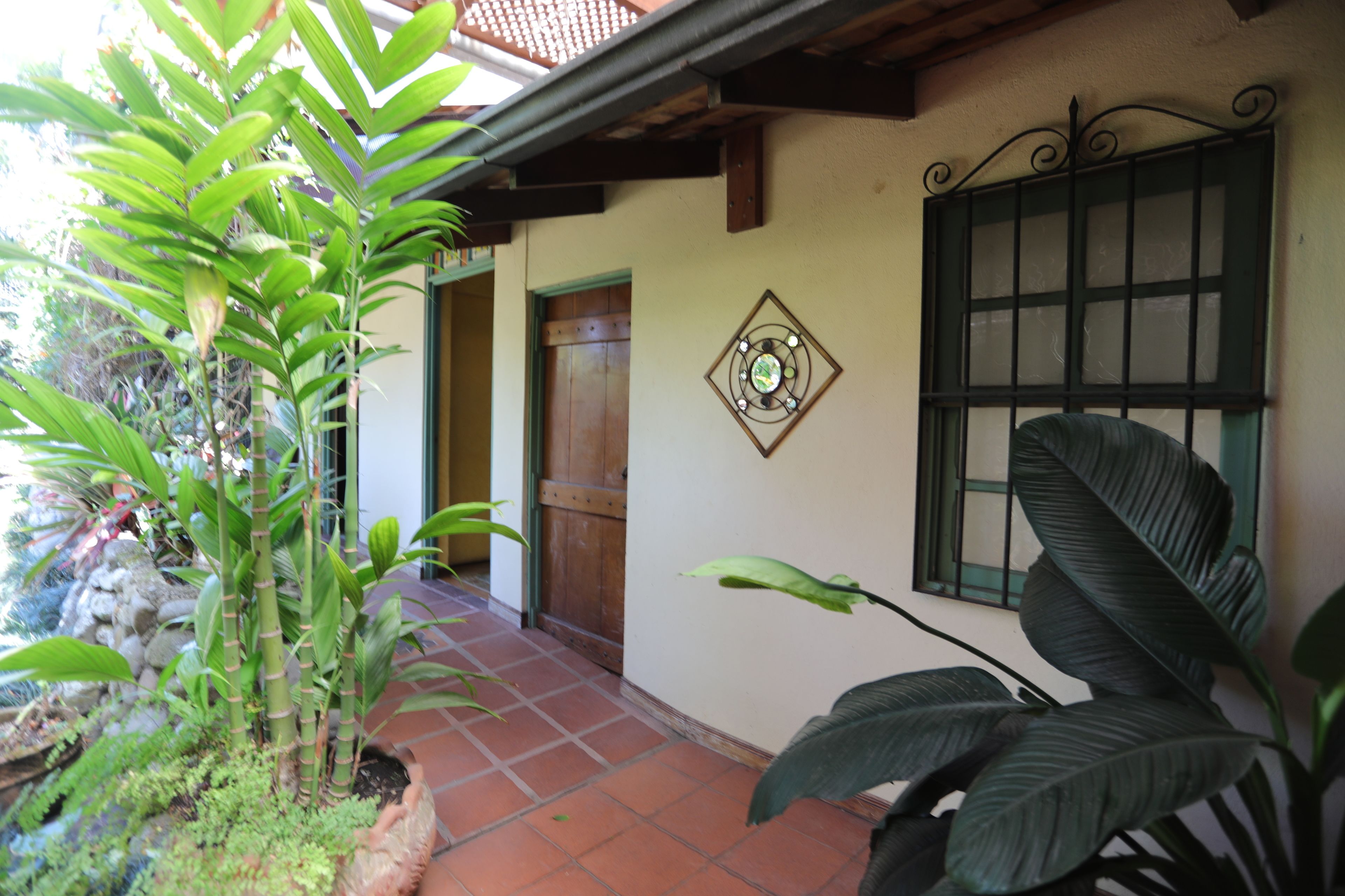 Um edifício com um pátio de azulejos, uma porta de madeira e uma janela com grade de metal.