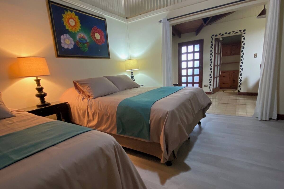 Une chambre avec deux lits, un tableau au mur et une porte donnant sur une autre pièce.