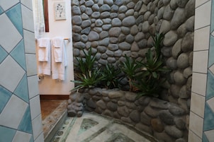 Un baño con pared de piedra, piso de baldosas y una planta pequeña.