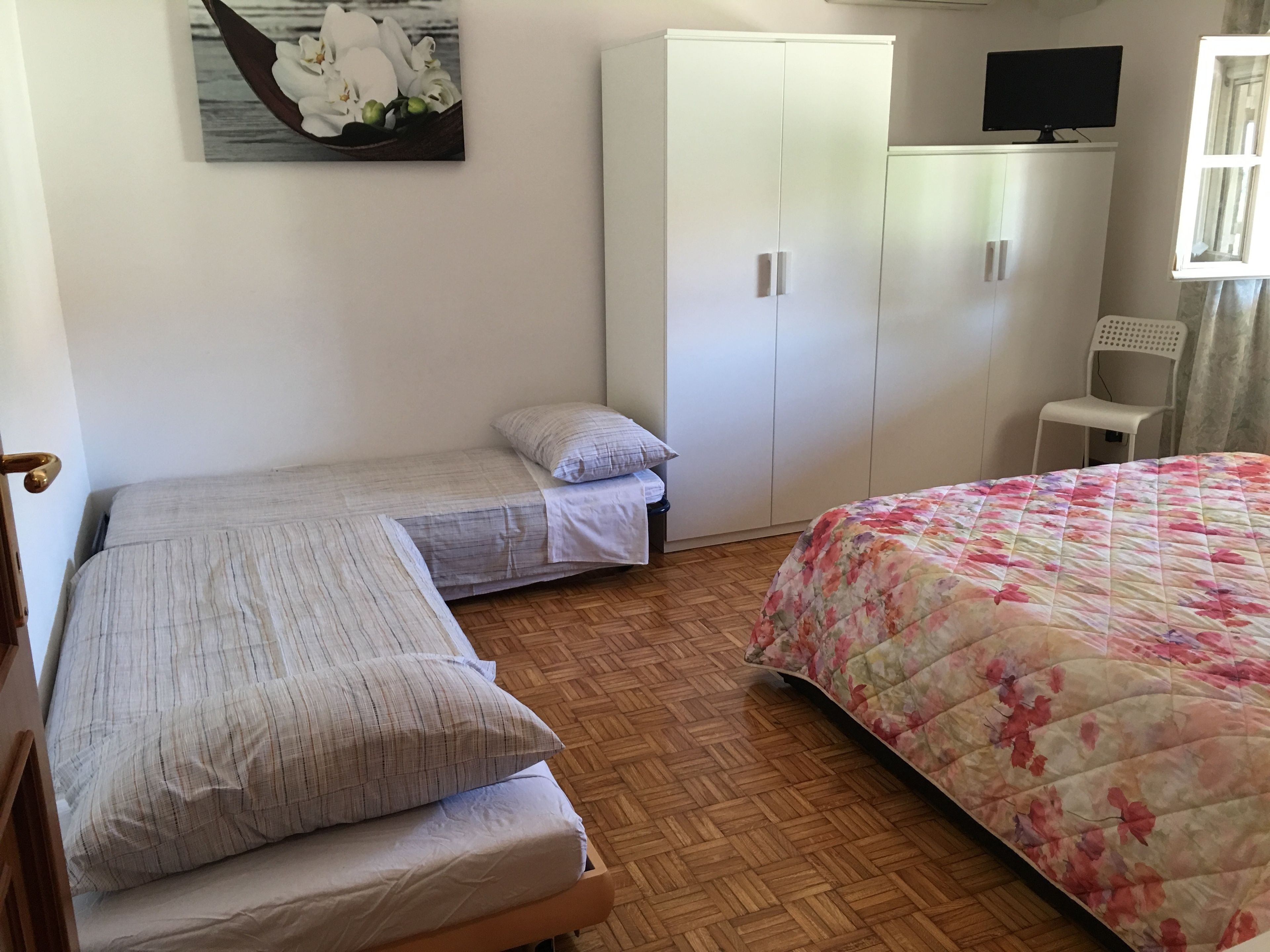 A bedroom with two single beds, a wardrobe, a television, and a chair.