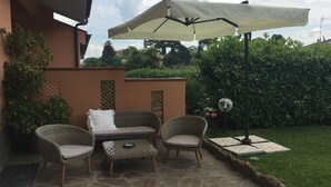 An outdoor patio with wicker furniture, a stone floor, and a large umbrella. - VillaGiò B&B (Frascati)