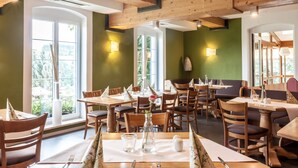 A restaurant with wooden tables and chairs, large windows, and a green wall. - Landhotel Gutshof (Hartenstein)