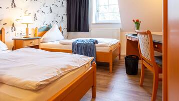 A hotel room with two single beds, a desk, a chair, a window with curtains, and a wall with a bird pattern.