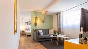 A modern living room with a grey sofa, a small round table, and a TV on a stand. - Landhotel Gutshof (Hartenstein)