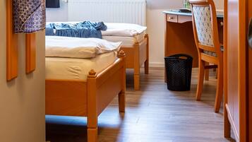 A bedroom with two wooden beds, a desk with a chair, a radiator, and a window with curtains.