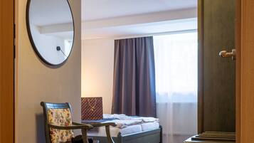 Habitación de hotel con cama, una silla, armario, espejo y ventana con cortinas.