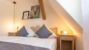 A bedroom with a large bed, two bedside tables, a nightstand, a wall-mounted picture, and a sloped ceiling. - Landhotel Gutshof (Hartenstein)