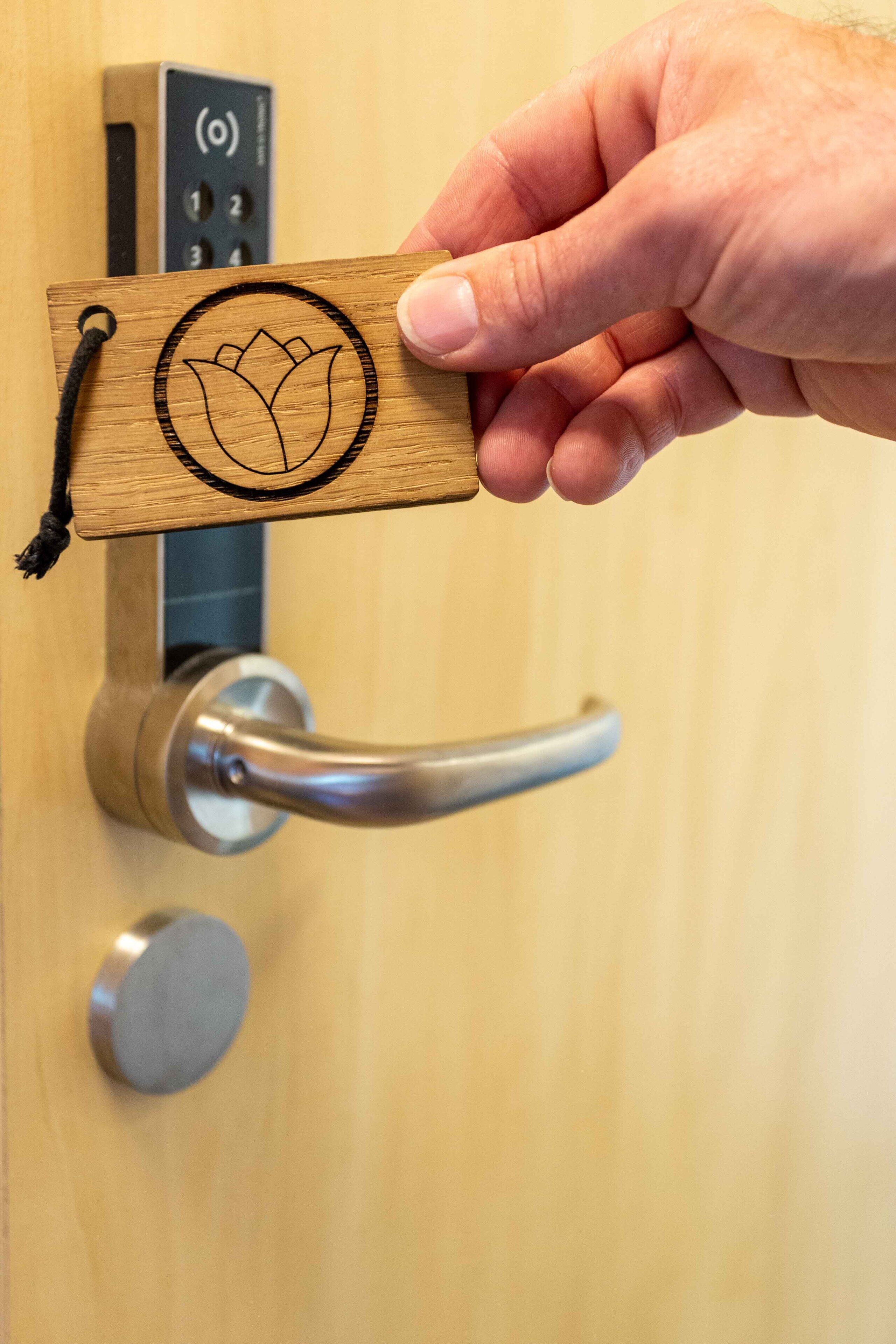 Una mano sostiene una tarjeta de madera con un diseño de flor de loto, colocada sobre una cerradura de puerta.