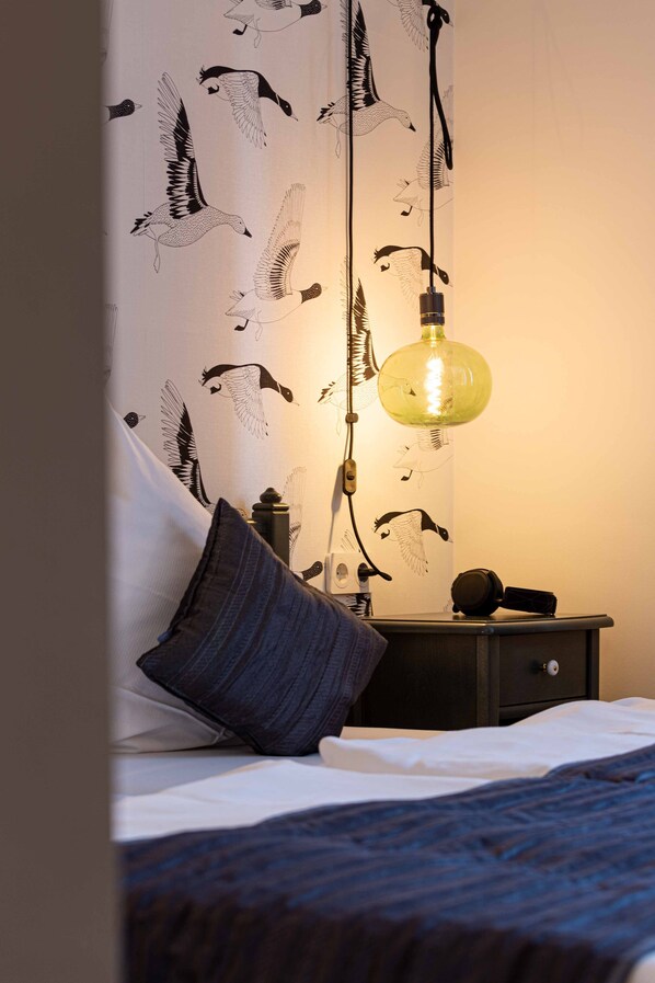 A bedroom with a bed, a nightstand, a lamp, and a wall with a bird pattern.