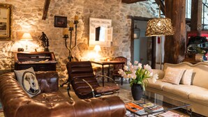 Un salón acogedor con pared de piedra, muebles de cuero, techo de madera y una lámpara colgante.