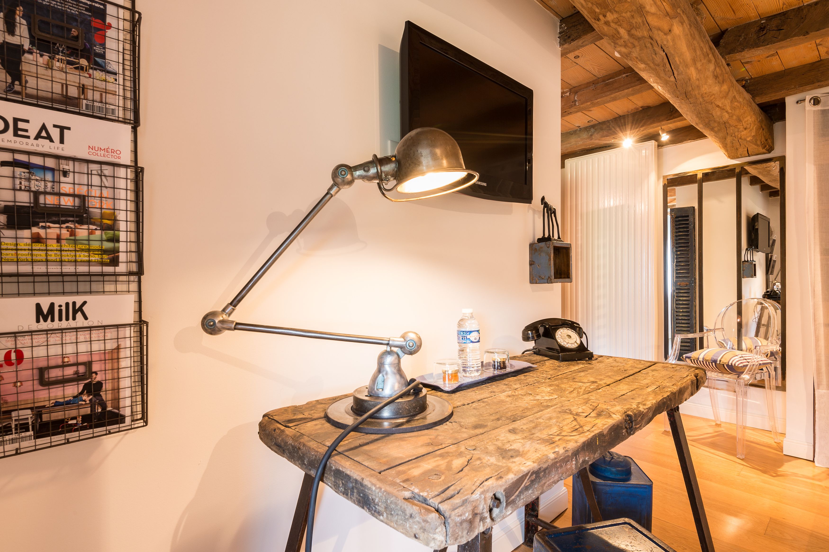 A rustic wooden table with a desk lamp, a water bottle, and a clock. There are wall-mounted cages with various items and a television.