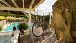 Una terraza de madera con un jacuzzi, una silla colgante y una estatua.
