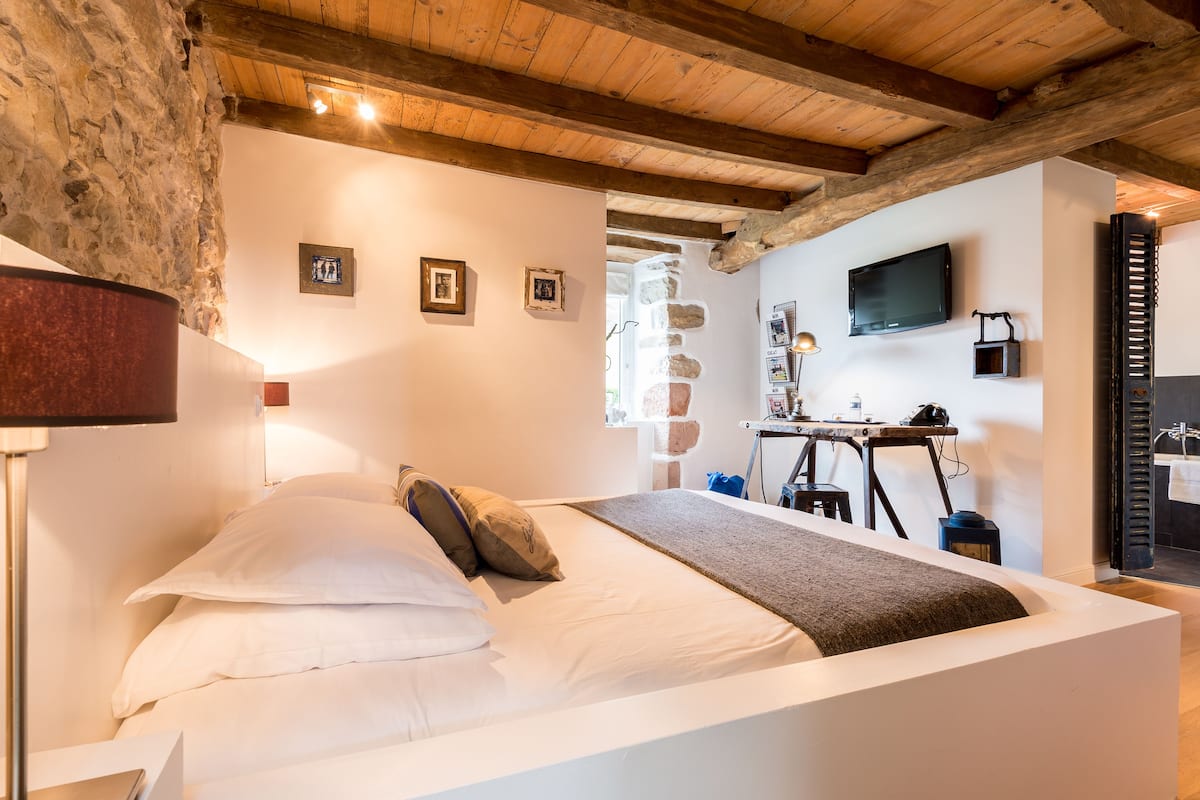 Un dormitorio con cama, lámpara, televisor y paredes de piedra.