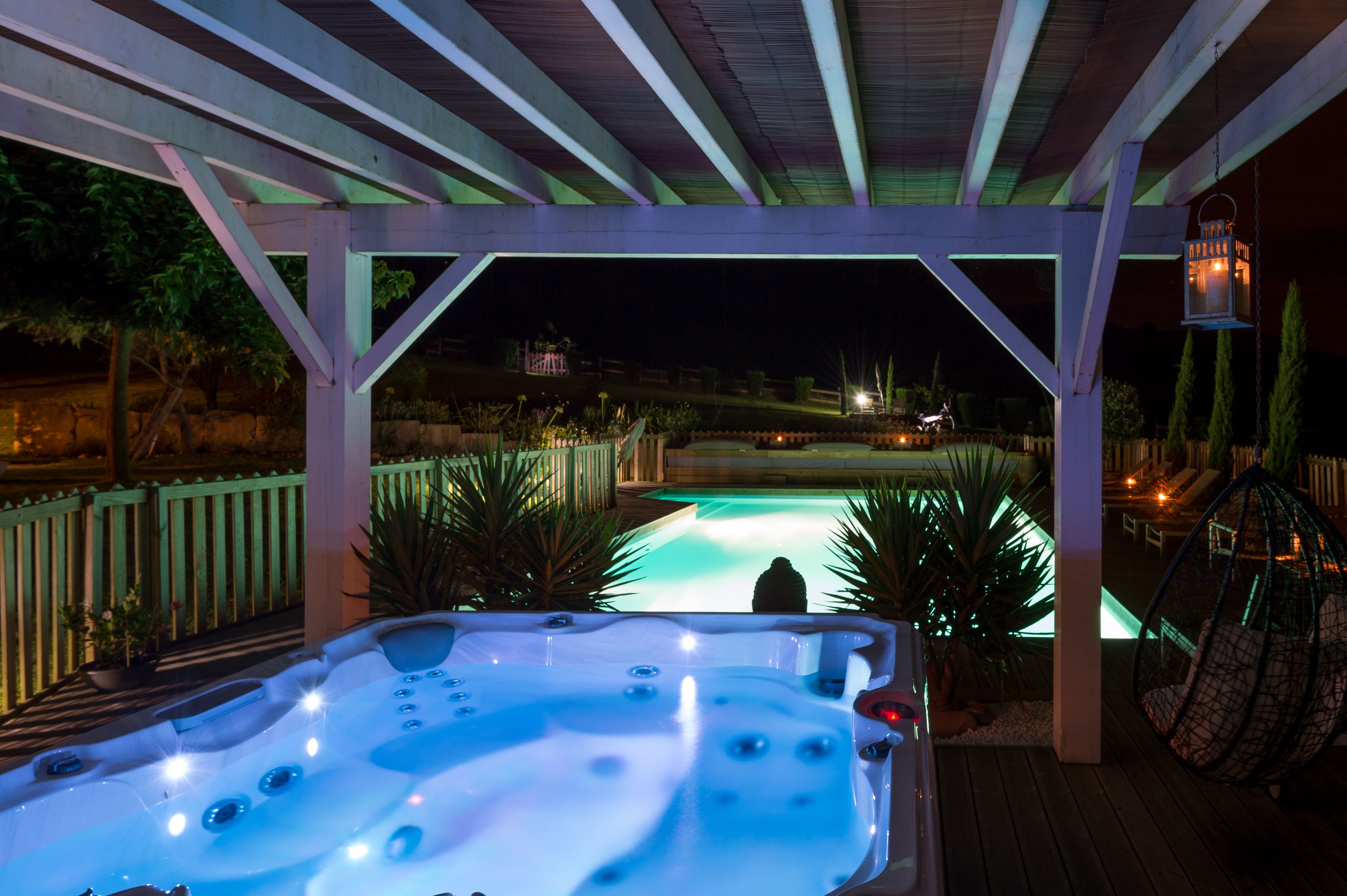 Ein Whirlpool unter einer Holz-Pergola mit Blick auf einen Pool bei Nacht.