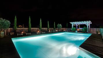 Una piscina con sillas de descanso y una pérgola de noche.