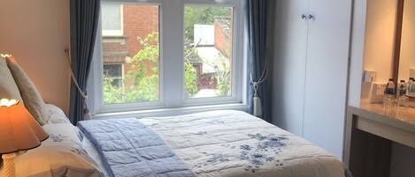 A bedroom with a large bed, a bedside table with a lamp, a wicker chair, and a wardrobe.